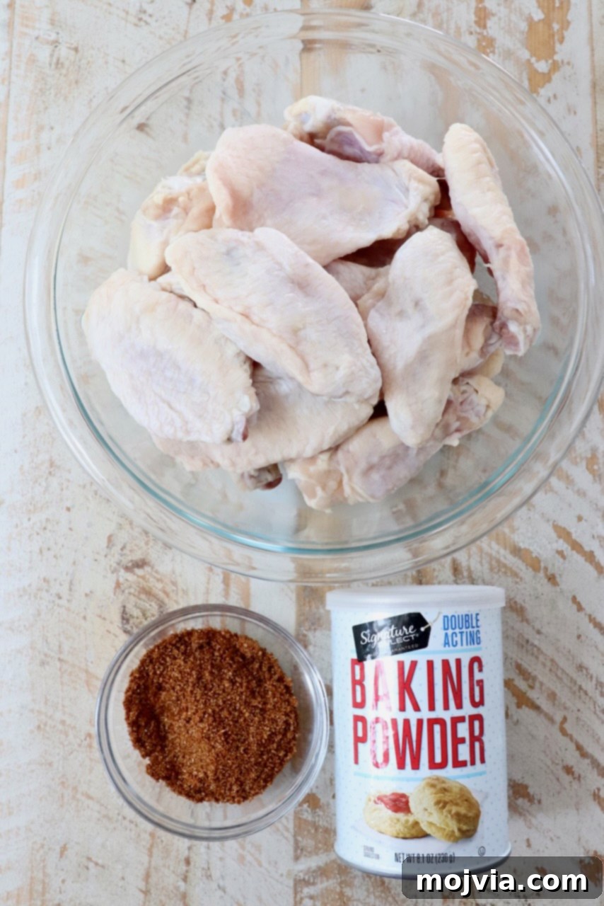 A collection of fresh ingredients for making Cajun wings, including chicken, spices, and sauce components, arranged on a rustic white wooden board.