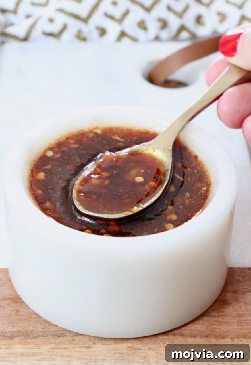 Sticky, Sweet, and Spicy General Tso Sauce 2 Hand holding a spoon dipped into a bowl of homemade General Tso sauce, showcasing its rich texture.