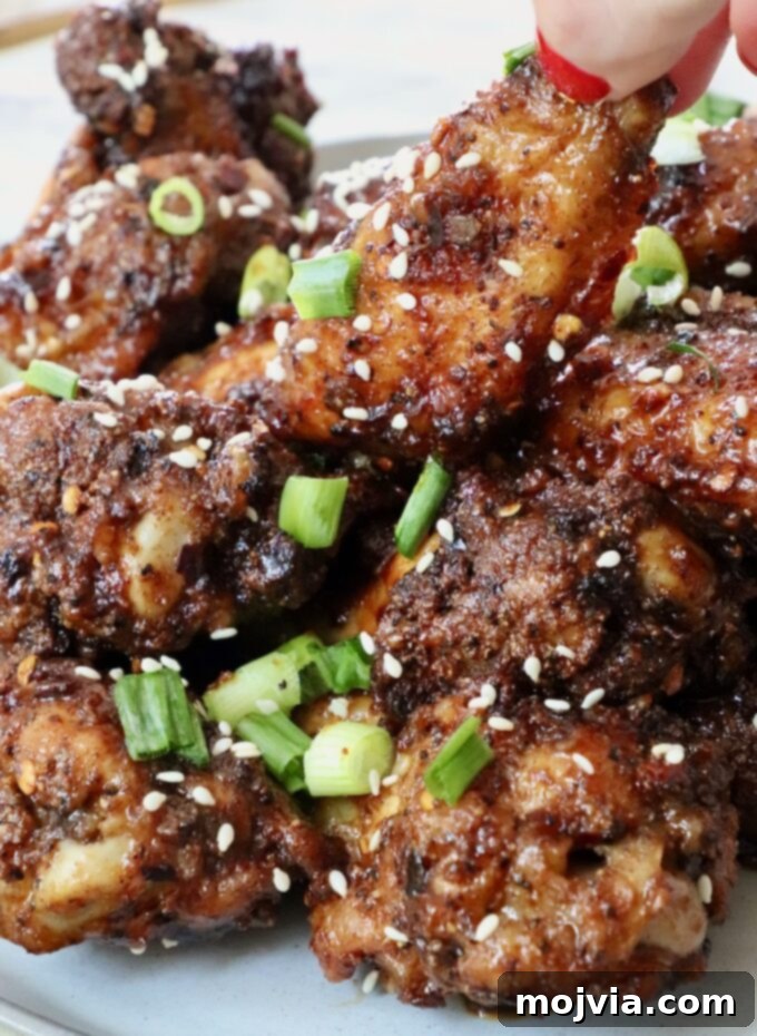 Sticky, Sweet, and Spicy General Tso Sauce 5 A hand reaching for a General Tso chicken wing, piled high with other saucy wings on a plate.