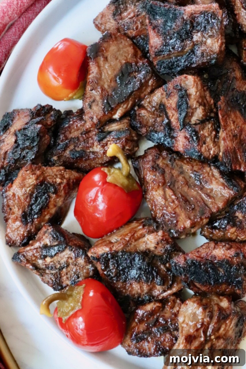 Grilled New England-style steak tips on a plate with vibrant cherry peppers, ready to be served