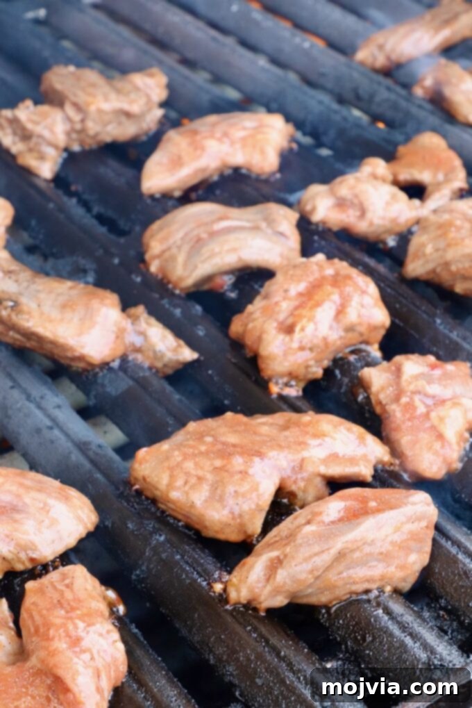 Marinated raw steak tips being placed onto a hot grill for searing