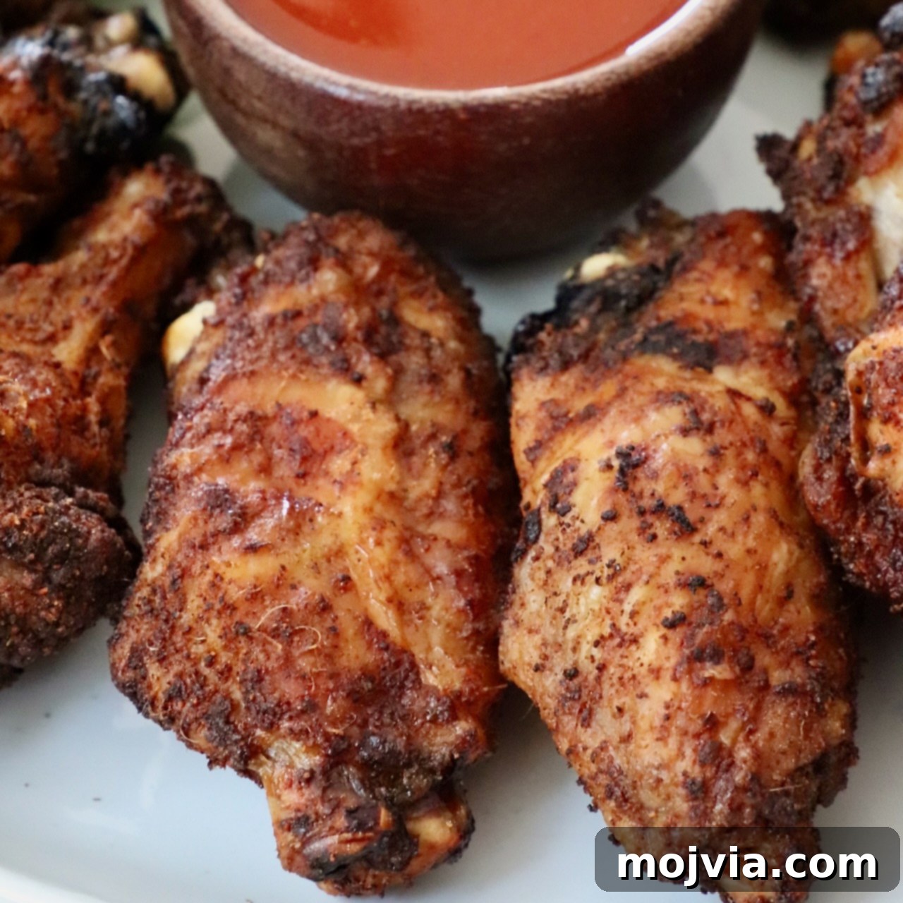 baked chicken wings on a plate with a small bowl of buffalo sauce