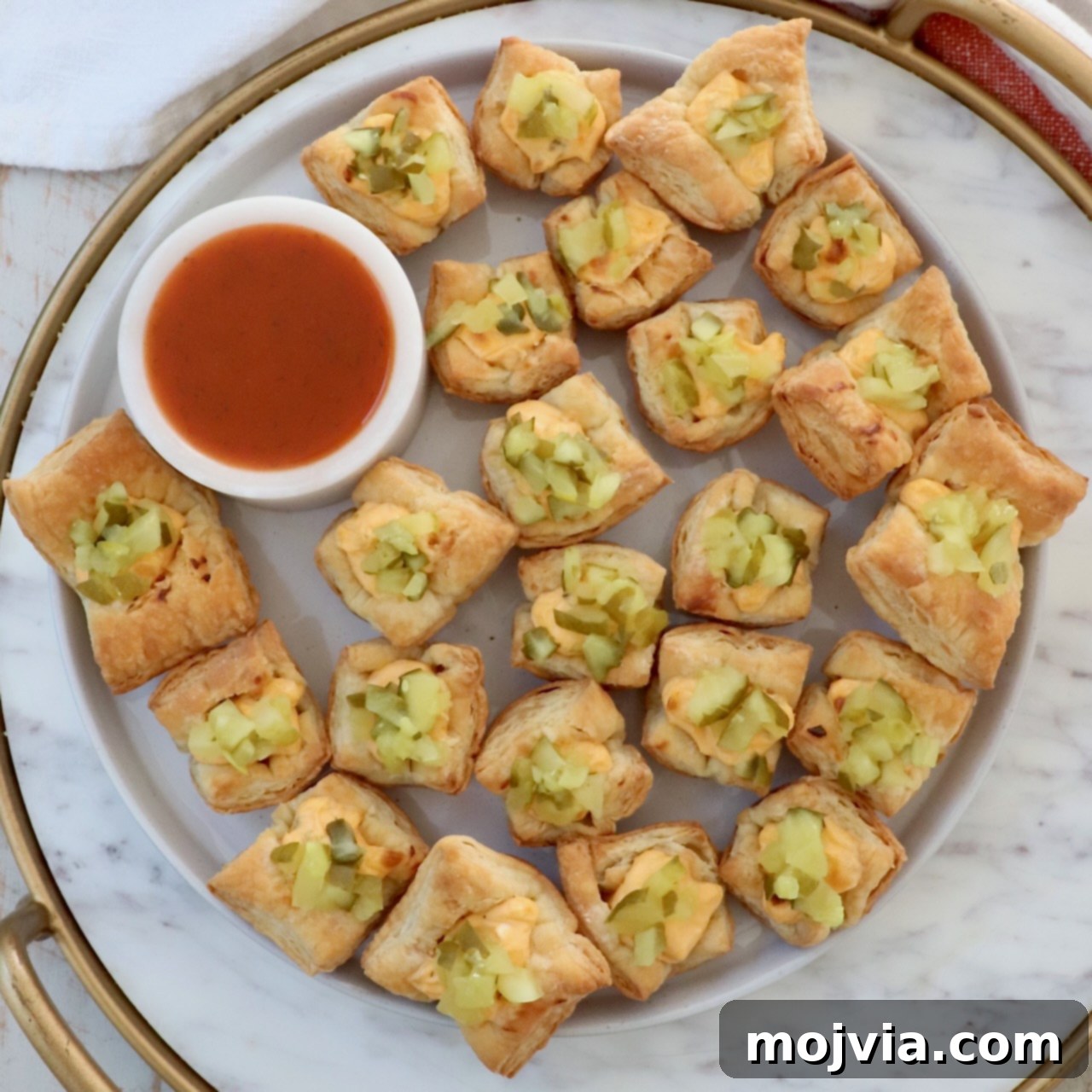 puff pastry pickles bites on a plate with a small bowl of hot sauce