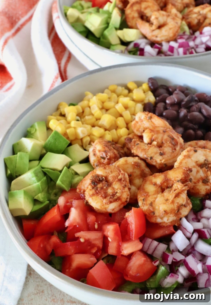 Fresh Fiesta Shrimp Salad 2 A colorful Mexican shrimp salad served in a bowl, featuring seasoned shrimp, diced avocado, red onions, black beans, corn, and cherry tomatoes atop fresh lettuce.