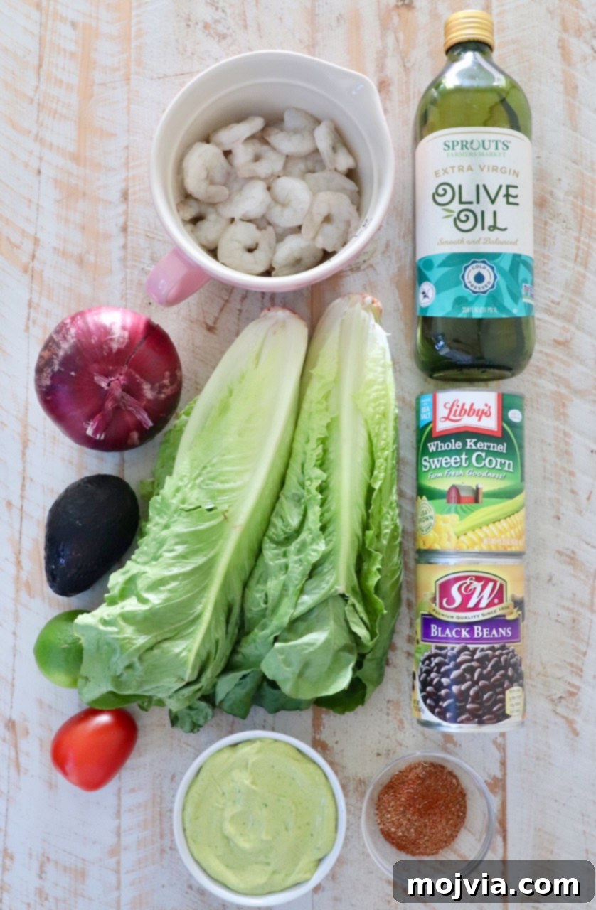Fresh Fiesta Shrimp Salad 3 A collection of fresh ingredients for Mexican shrimp salad laid out on a white wooden board, including romaine lettuce, red onion, black beans, corn, roma tomatoes, avocados, and raw shrimp.