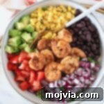 A beautifully presented Mexican shrimp salad in a bowl, with a fork, ready to be eaten. It features succulent shrimp, avocado, red onion, tomato, black beans, and corn.