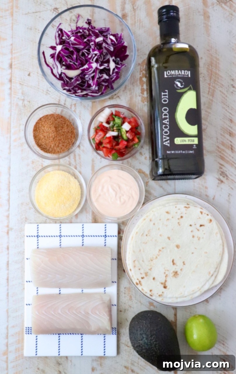 A top-down, beautifully styled flat lay of all the essential ingredients for air fryer fish tacos. Featured prominently are fresh red cabbage, a bottle of avocado oil, taco seasoning, a bowl of vibrant pico de gallo, a small container of fish taco sauce, cornmeal, a stack of tortillas, raw fish fillets, a perfectly ripe avocado, and a bright green lime. All elements are arranged artfully on a light wooden surface, highlighting the freshness and readiness of the components.
