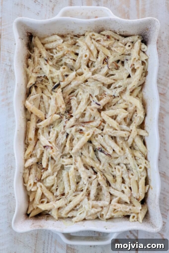 Golden French Onion Boursin Pasta 7 Creamy baked penne pasta in a white rectangular dish on a light wooden table.