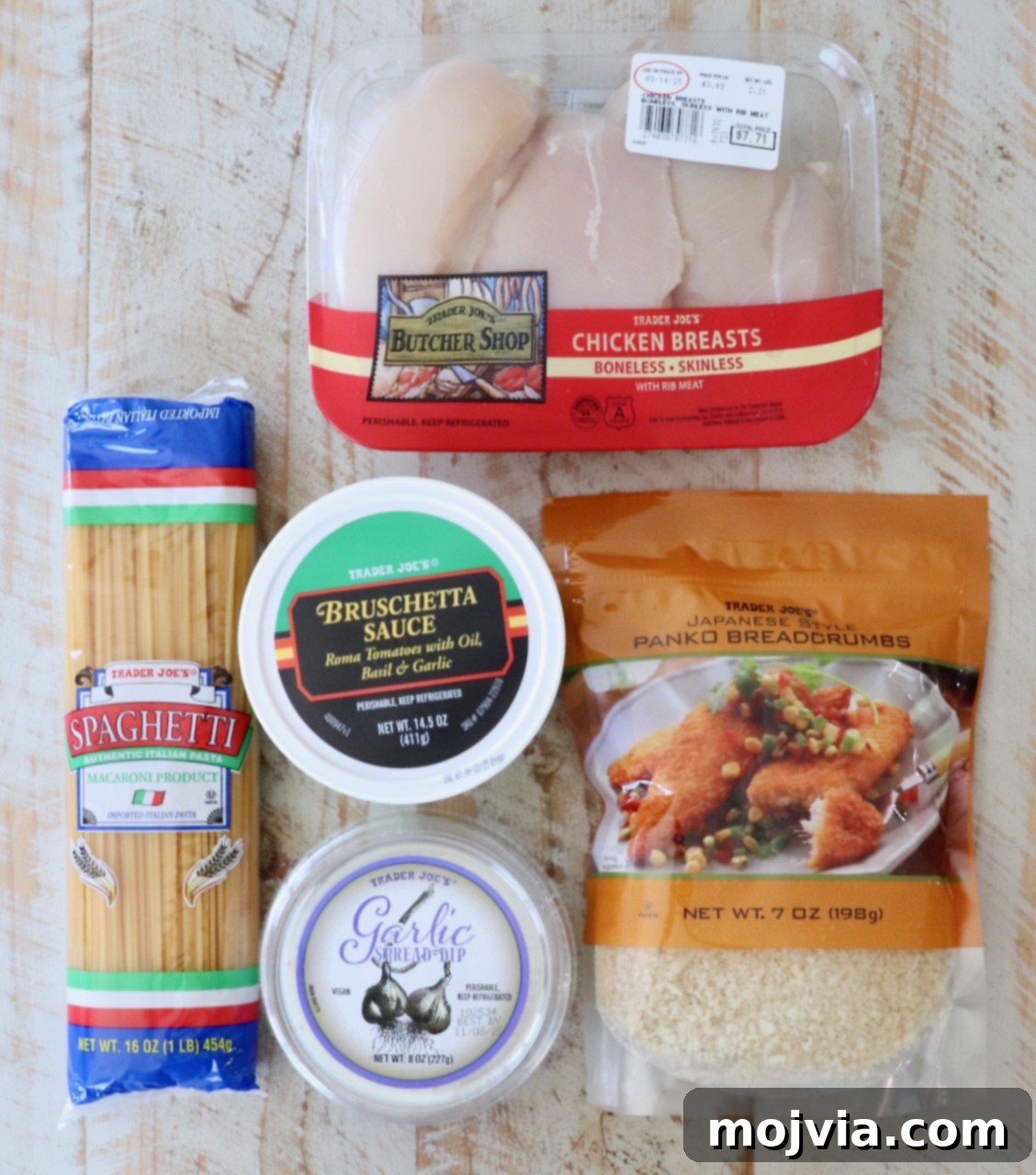 A vibrant selection of Trader Joe's recipe ingredients neatly arranged on a rustic wooden surface: boneless chicken breasts, a jar of classic bruschetta sauce, a bundle of spaghetti noodles, a tub of creamy garlic spread, and a bag of crunchy panko breadcrumbs.