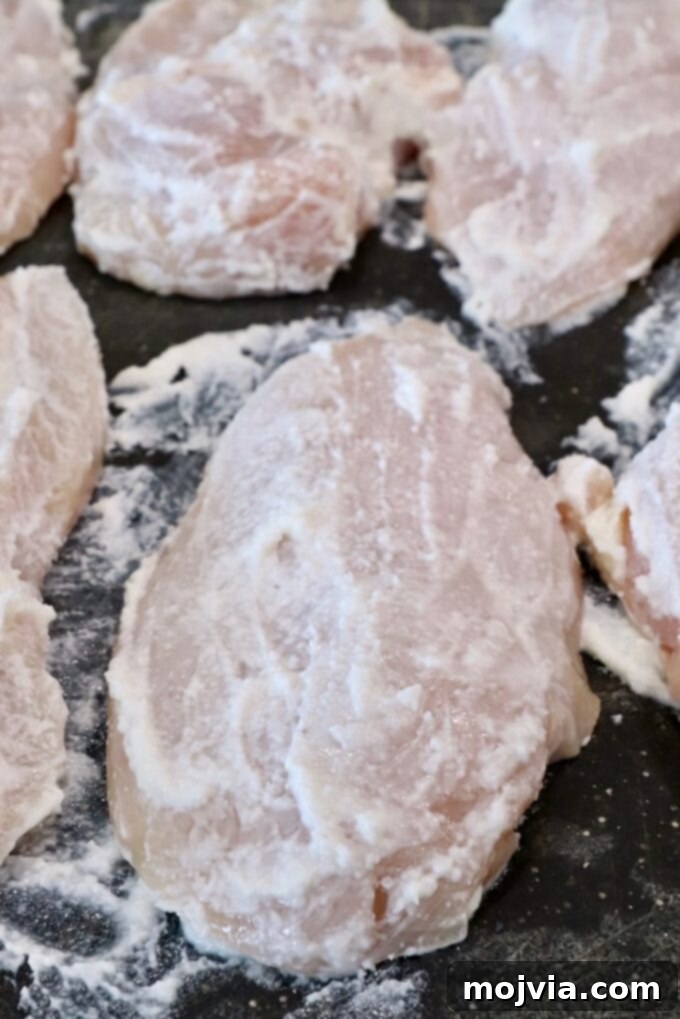 Raw chicken breasts generously coated in a rich garlic spread, resting on a clean cutting board, ready for the next step.