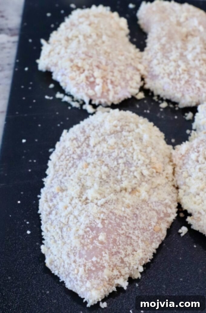 Flattened chicken breasts, now perfectly coated with crunchy panko breadcrumbs, arranged on a cutting board, prepared for cooking.