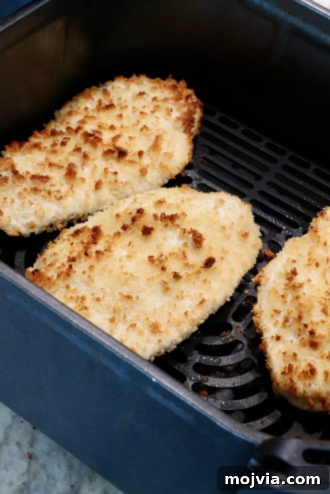 Golden-brown, perfectly crispy chicken breasts, freshly cooked and still hot, resting inside an air fryer basket after achieving optimal crispiness.