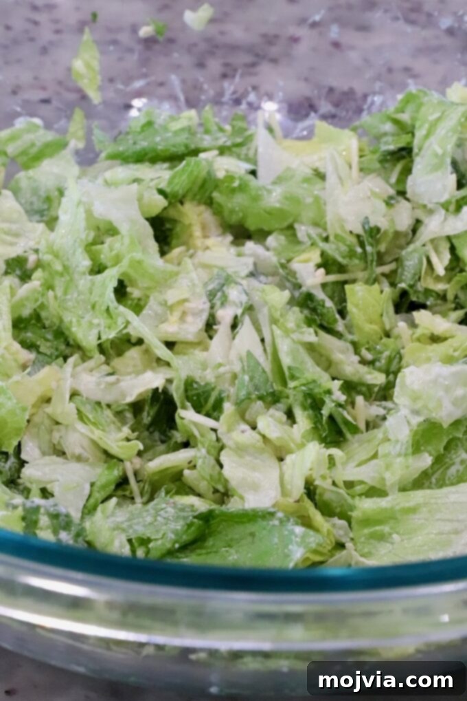 Chopped lettuce with grated cheese in a glass bowl on a speckled countertop. 