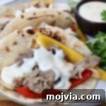 Grilled steak with yellow and red bell peppers, topped with creamy white queso in charred tortillas. Garnished with fresh cilantro on the side and a cup of queso on the side.