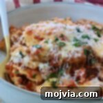 Cheesy Baked Ravioli Delight 12 Close-up of a bowl of baked ravioli with melted cheese, garnished with fresh herbs with a fork in the bowl. Behind it, a red-striped cloth.