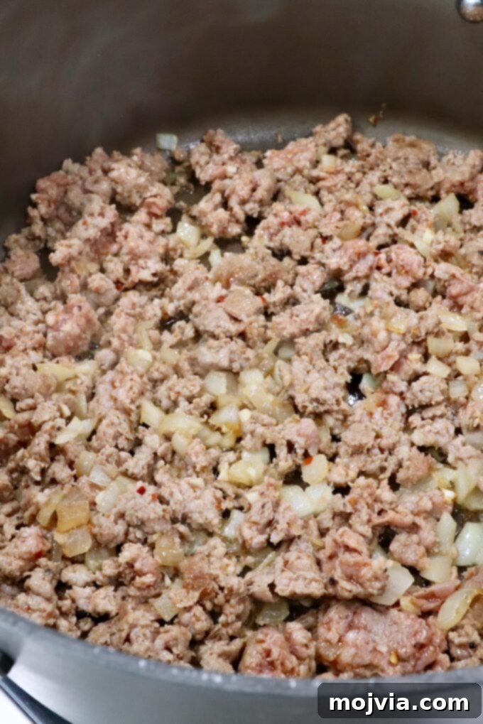 Cheesy Baked Ravioli Delight 4 Ground meat is being browned with onions in a large skillet.