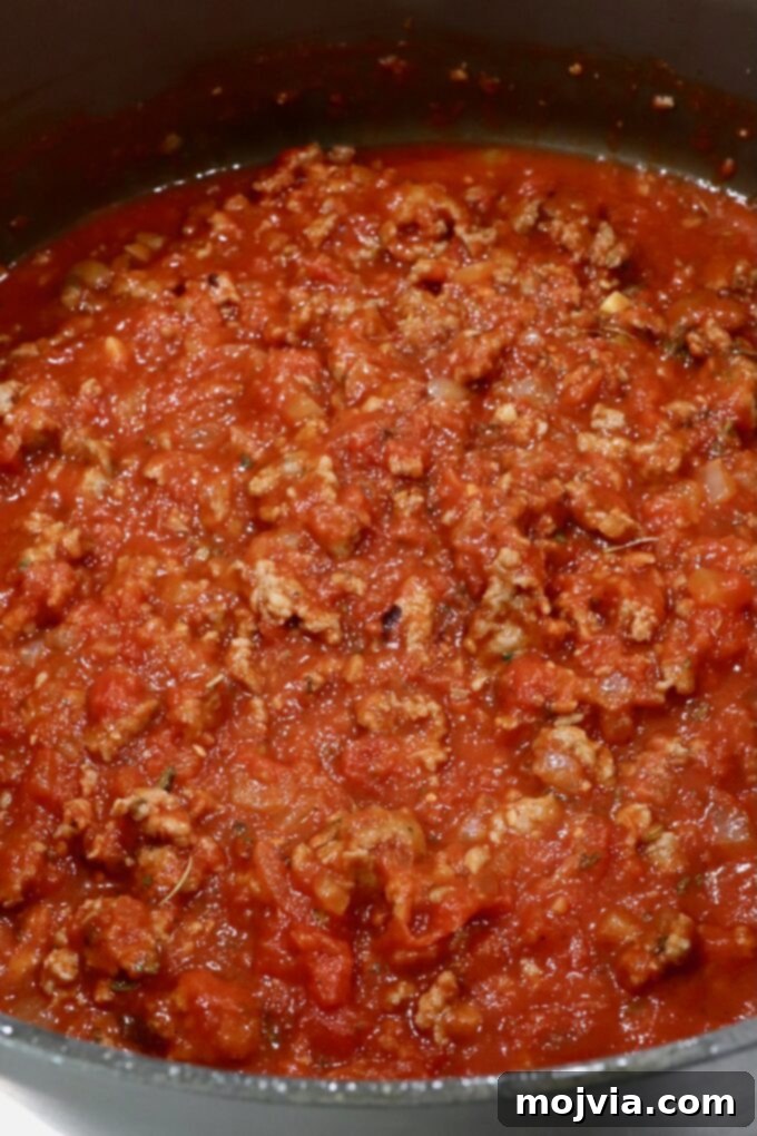 Cheesy Baked Ravioli Delight 5 Close-up of a simmering pot of rich red tomato meat sauce, featuring ground meat and diced tomatoes