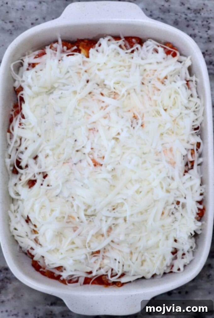 Cheesy Baked Ravioli Delight 9 A casserole dish filled with baked ravioli, topped generously with shredded cheese. The cheese covers a layer of tomato sauce.