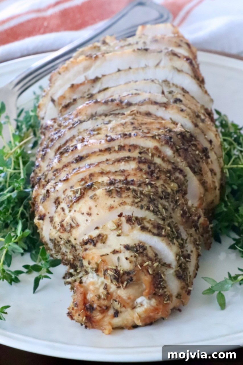 Perfect Air Fried Turkey Breast 2 Sliced herb-crusted roast turkey breast on a white plate, surrounded by fresh green herbs.