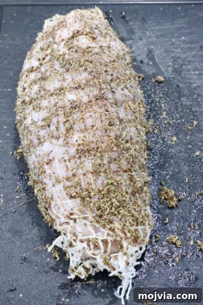 Perfect Air Fried Turkey Breast 4 turkey breast roast wrapped in netting, covered in an herb rub on a black cutting board