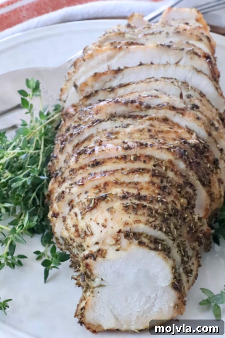 Perfect Air Fried Turkey Breast 7 Sliced herb-crusted roast turkey breast on a white plate, surrounded by fresh green herbs.
