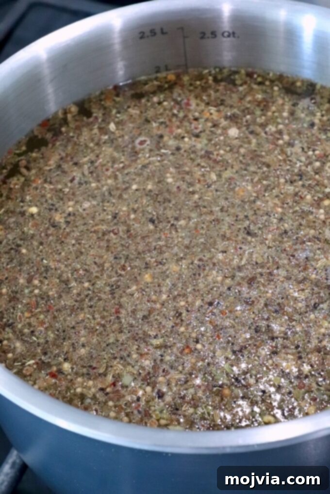 A silver pot filled with a simmering mixture of seeds and spices in liquid