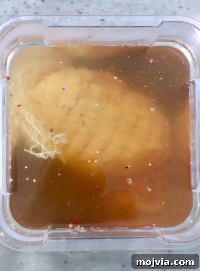 A turkey breast is submerged in a light brown brine within a plastic container. 