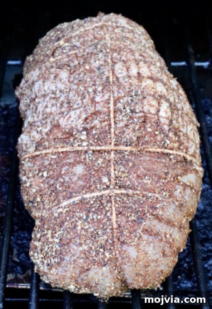 Seasoned turkey breast tied with string on a smoker. The meat is coated with spices, creating a textured surface