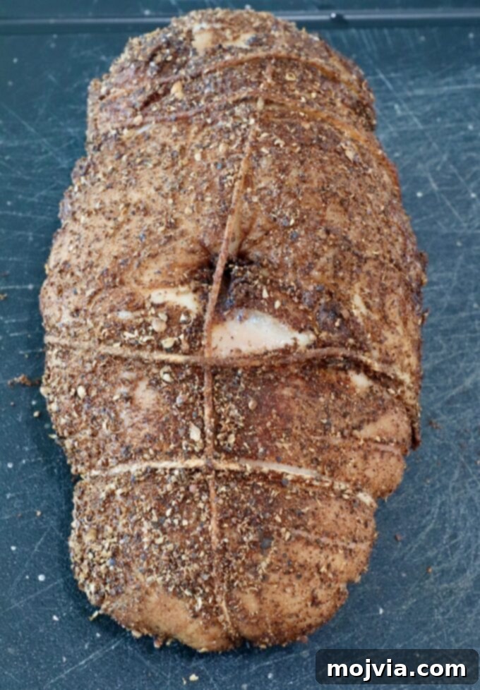 turkey breast tied with twine, coated in a dark, textured spice rub, lies on a black cutting board.