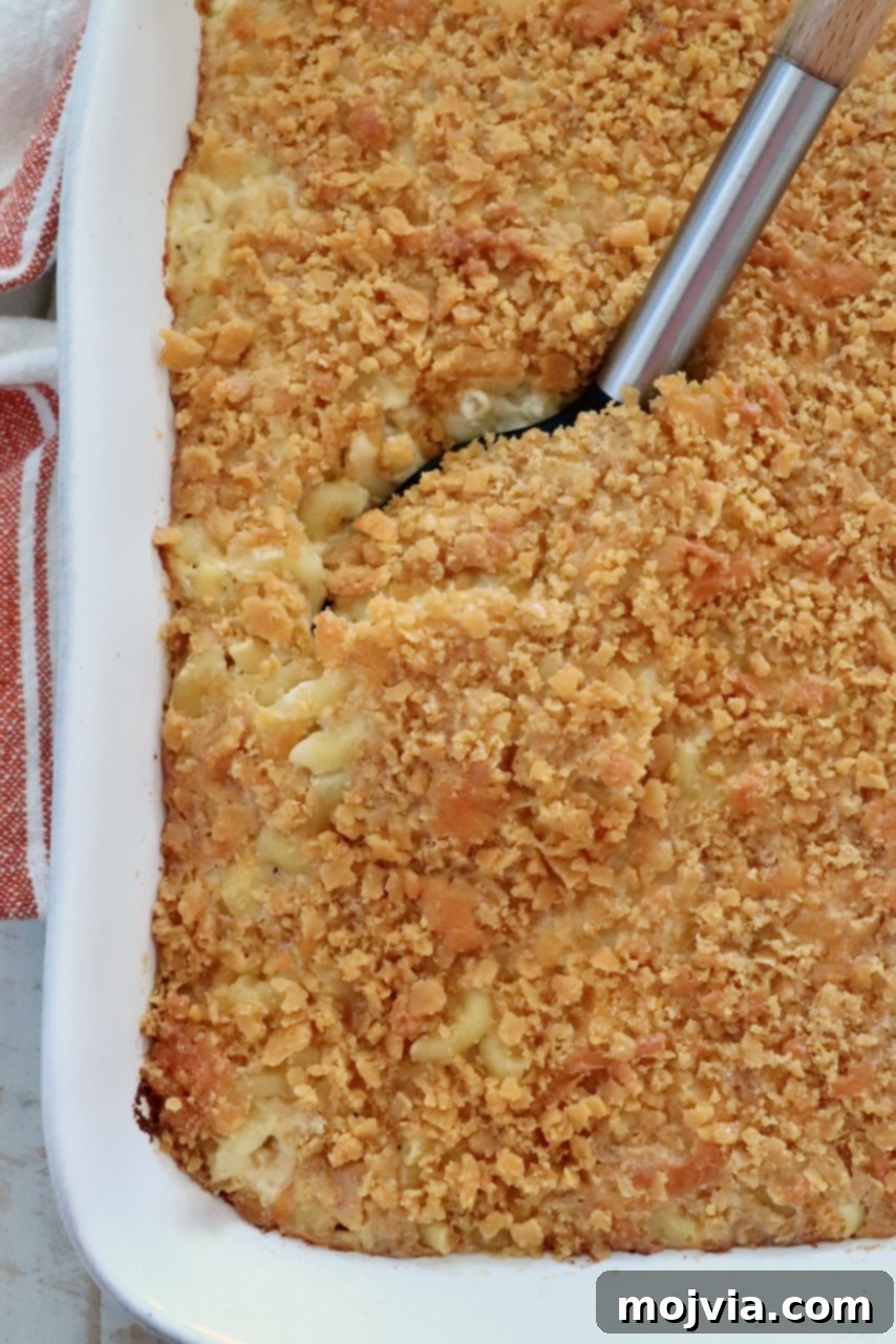 Golden Cheez-It Mac and Cheese Bake 2 Golden-brown baked macaroni and cheese with a crispy cracker topping in a white casserole dish. A serving spoon is lifting a portion, revealing creamy pasta underneath.