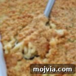 Close-up of creamy macaroni and cheese topped with golden, crispy Cheez-It cracker topping. A serving spoon is lifting up a portion, revealing gooey cheese beneath.