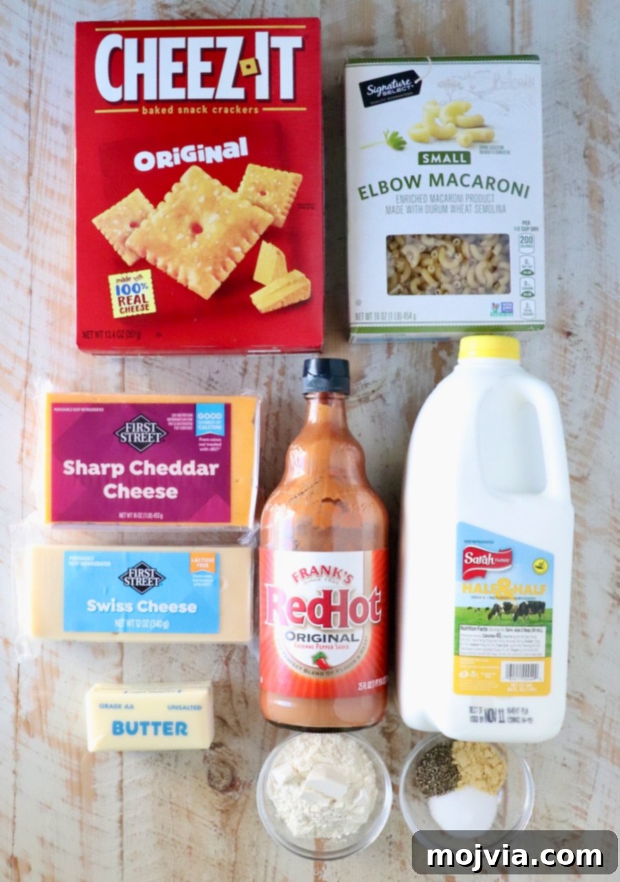 Golden Cheez-It Mac and Cheese Bake 3 Assorted ingredients for mac and cheese on a wooden surface, including a box of Cheez-It crackers, elbow macaroni, cheddar and Swiss cheeses, hot sauce, milk, butter, flour, and spices.