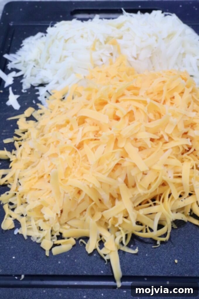 Golden Cheez-It Mac and Cheese Bake 4 A pile of finely grated swiss cheese and a separate pile of cheddar cheese are on a black cutting board