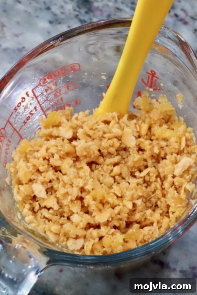 Golden Cheez-It Mac and Cheese Bake 10 A clear measuring cup filled with crumbled Cheez-Its sits on a marble countertop. A bright yellow spoon is partially immersed in the crushed crackers.