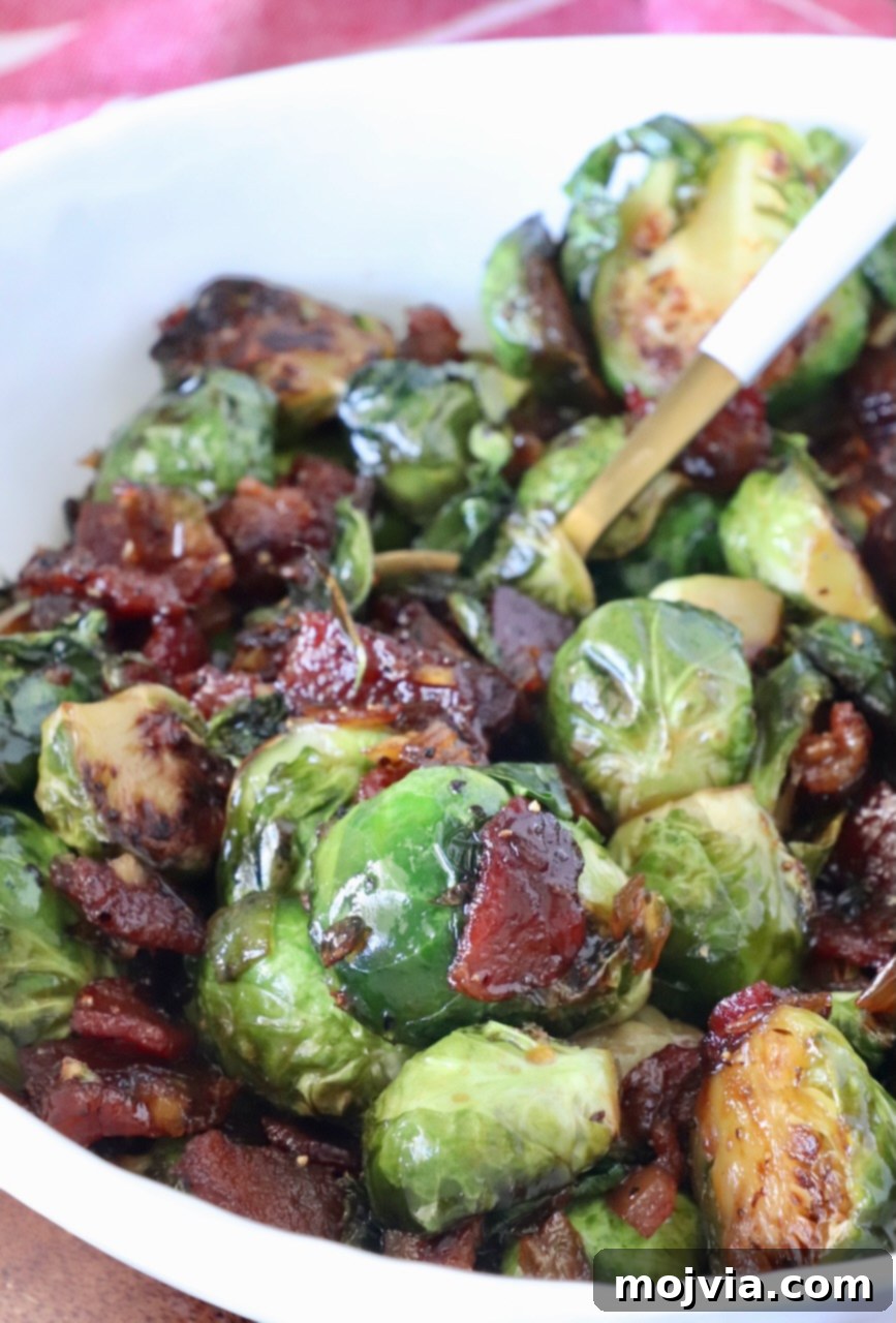 Sticky Bacon Brussels Sprouts 2 Caramelized Brussels sprouts with crispy bacon pieces in a white bowl. The sprouts are glazed, showing a glossy texture.