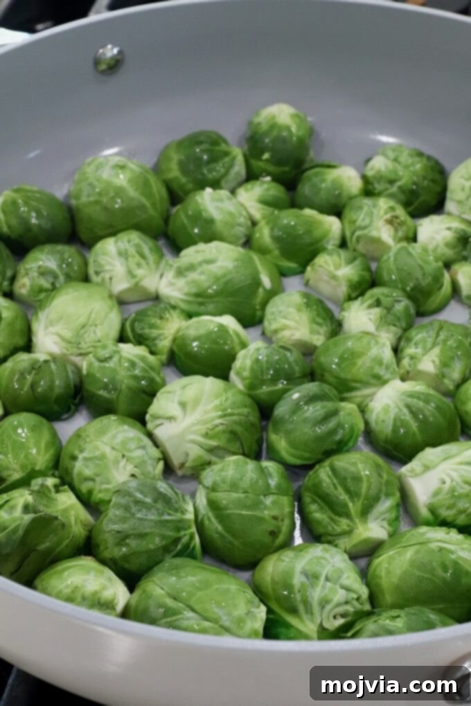 Sticky Bacon Brussels Sprouts 4 Fresh green Brussels sprouts evenly spread in a light-colored frying pan