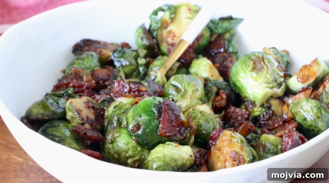 Sticky Bacon Brussels Sprouts 8 A white bowl filled with caramelized Brussels sprouts mixed with crispy bacon pieces, glistening with glaze, and a spoon for serving.