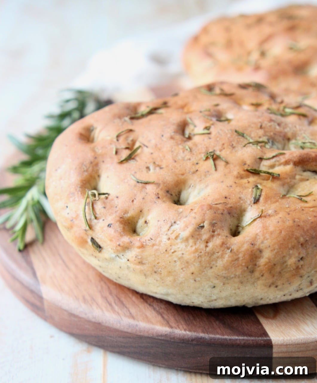Fragrant Rosemary Focaccia 2 Rosemary focaccia bread on wood cutting board with fresh rosemary sprigs