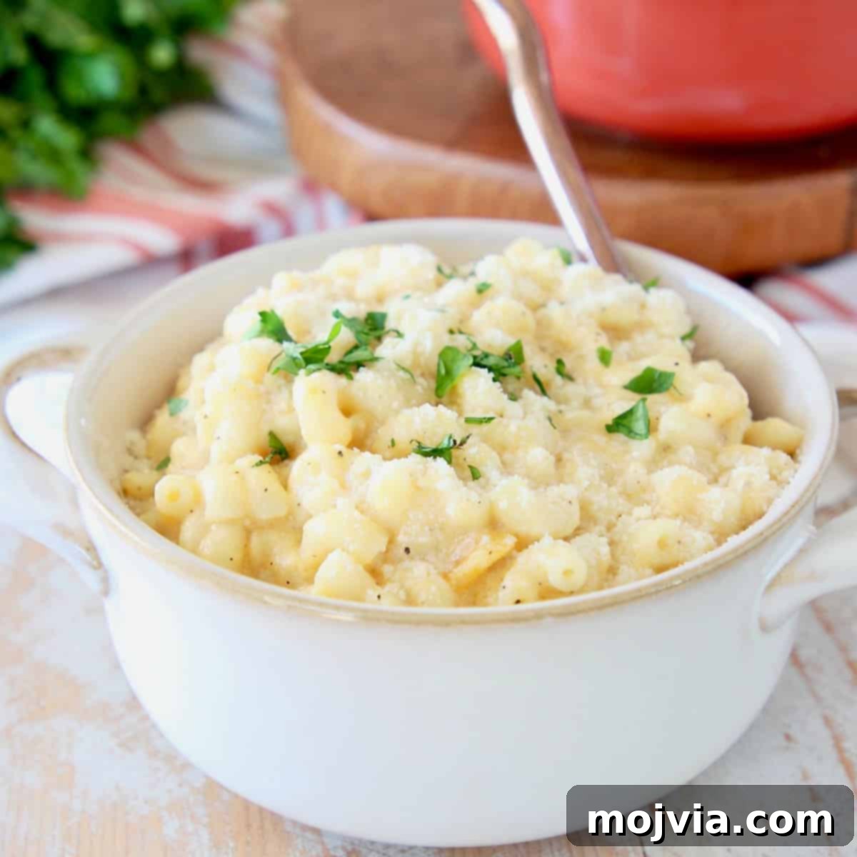 Butternut squash mac and cheese in white bowl with gold spoon on orange striped towel with fresh parsley