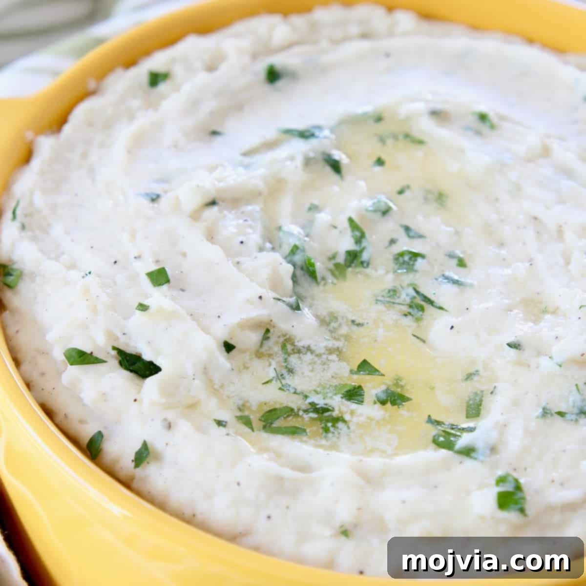 Mashed potatoes topped with melted butter and chopped parsley in yellow bowl