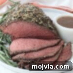 Tender Sirloin Tip Roast 10 Roast beef topped with herbs and spices, sliced to reveal a juicy pink interior. Garnished with rosemary and served on a white plate with gravy.