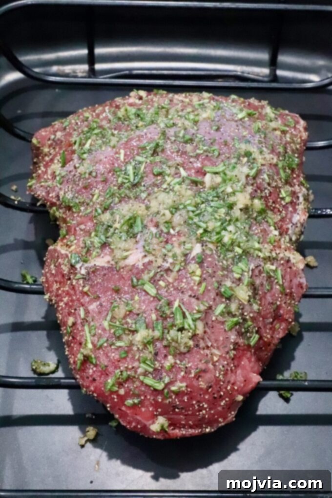 Tender Sirloin Tip Roast 4 Raw seasoned beef roast covered in chopped herbs and spices, resting in a roasting pan.