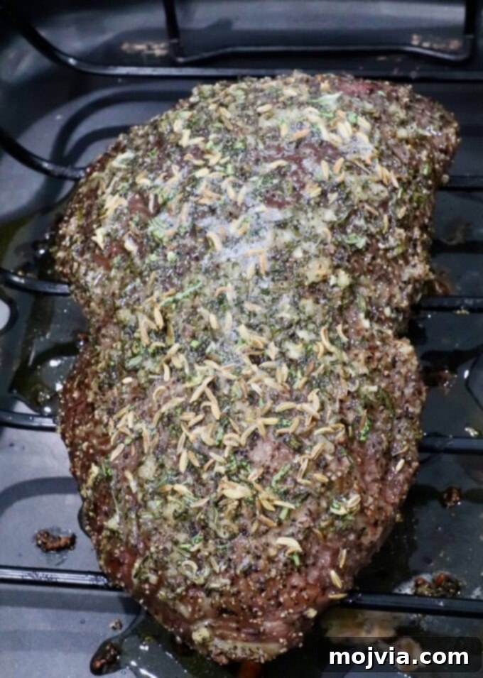 Tender Sirloin Tip Roast 6 A seasoned roast beef resting on a wire rack, topped with herbs and spices, in a dark roasting pan