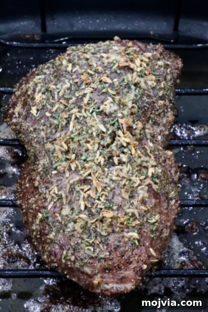 Tender Sirloin Tip Roast 7 A seasoned roast beef resting on a wire rack, topped with herbs and spices, in a dark roasting pan