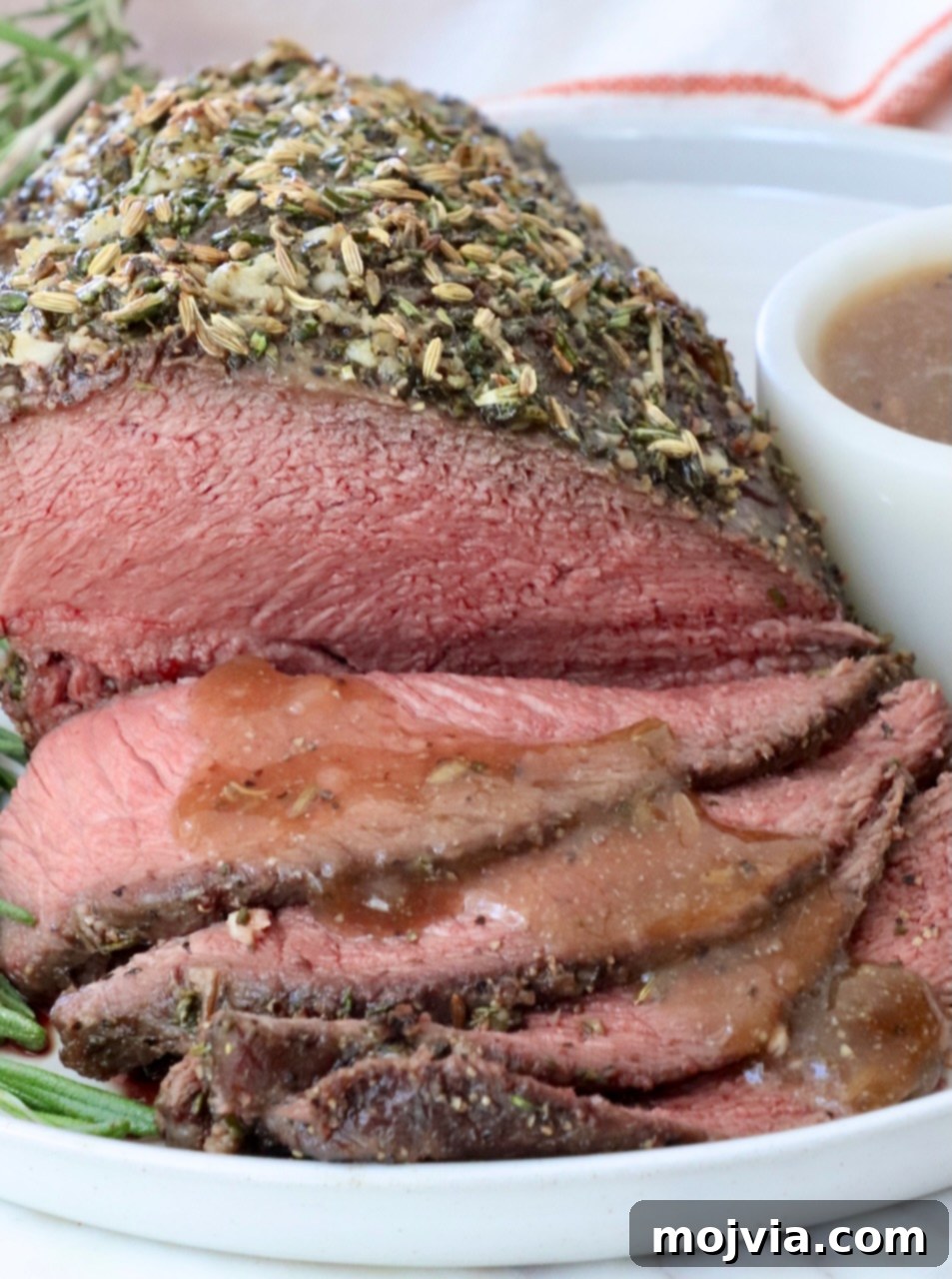 Tender Sirloin Tip Roast 8 Herb-crusted roast beef, thinly sliced and served on a white plate with brown gravy drizzled over the slices of beef.