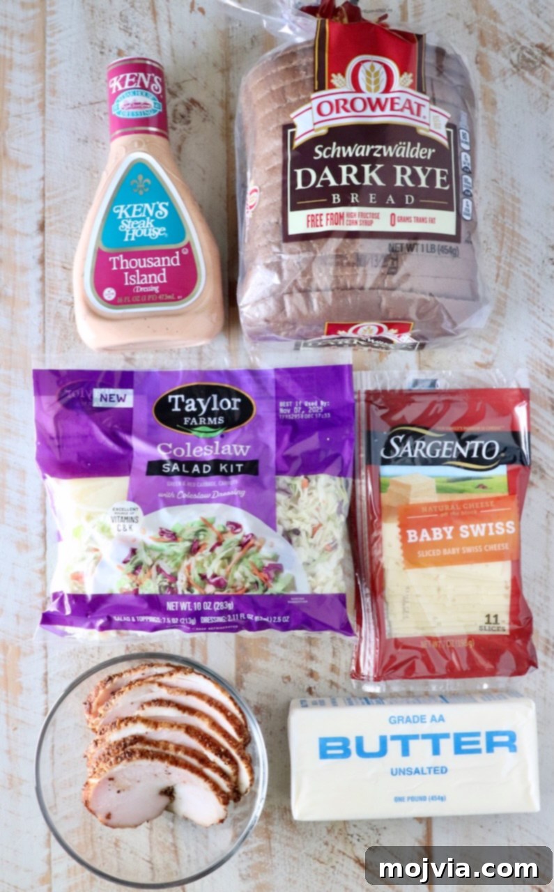 Golden Grilled Turkey Reuben 3 Packaged ingredients on a wooden table include Thousand Island dressing, dark rye bread, coleslaw kit, baby Swiss cheese, sliced cooked turkey, and butter.