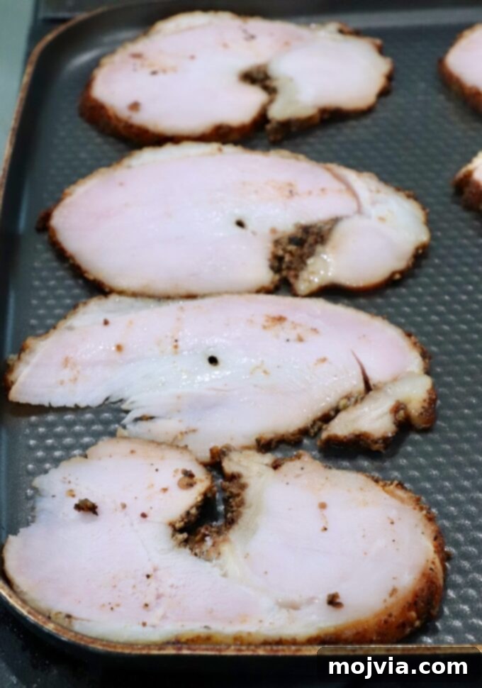 Golden Grilled Turkey Reuben 4 Slices of roasted turkey breast with a browned seasoning crust are laid out on a textured skillet.