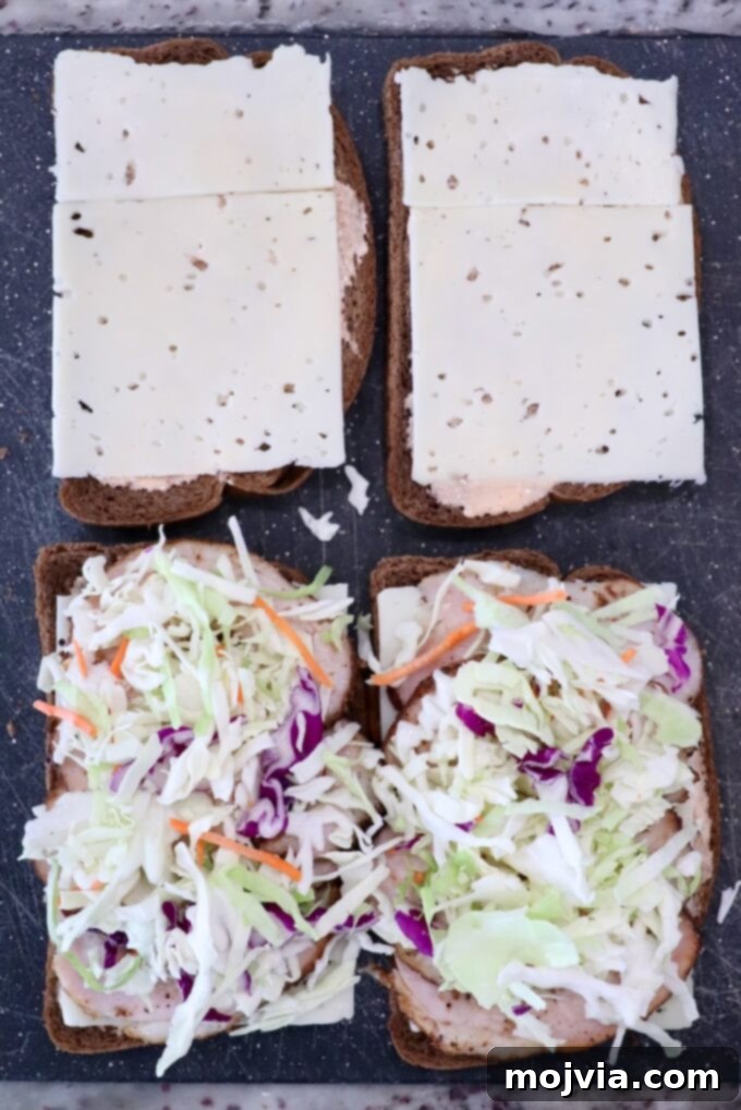 Golden Grilled Turkey Reuben 5 Open rye bread sandwiches: two with sliced cheese, two with coleslaw and meat, on a dark surface.