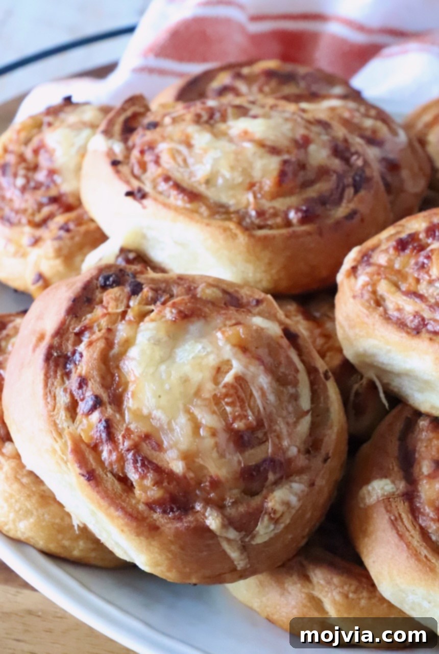 Savory French Onion Bites 2 Close-up of golden-brown cheese and onion buns on a white plate. The swirled bread shows a crispy texture, indicating a delightful combination of flaky pastry and savory filling.