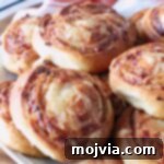 Close-up of golden-brown french onion rolls on a white plate. The swirled bread shows a crispy texture, revealing a tantalizing glimpse of the cheesy onion filling.